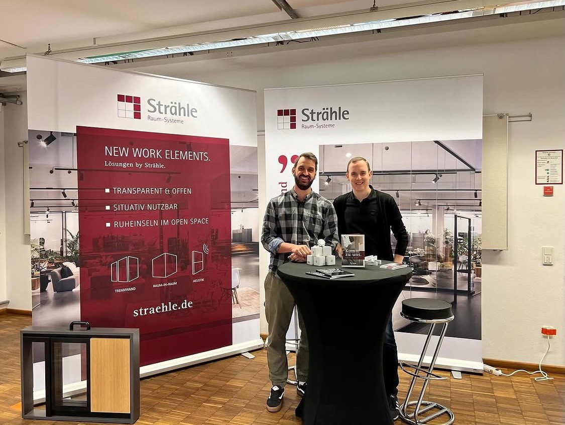 Zwei Männer präsentieren vor einer Straühle Ausstellung zu modernen und modularen Bürokonzepten.