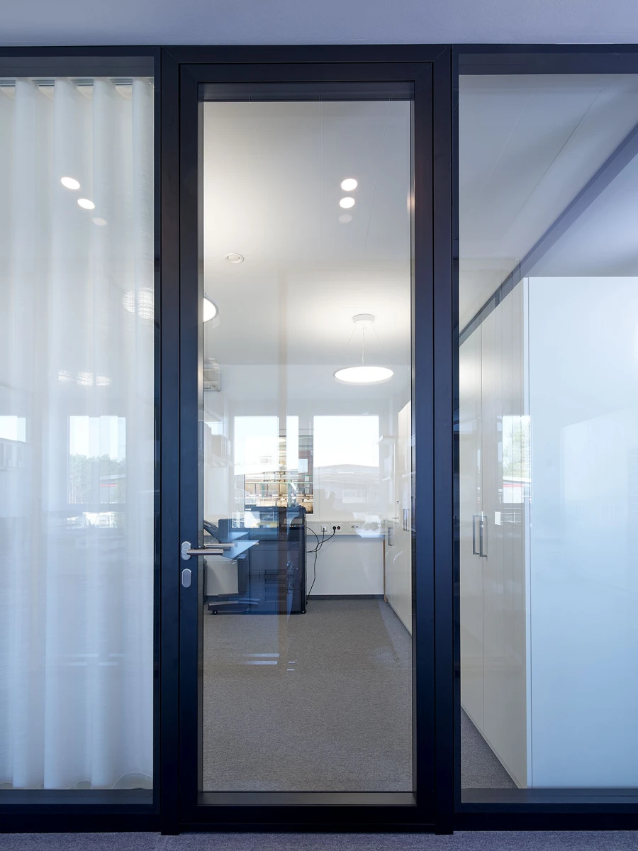 Blick durch eine große, schwarze Glastür auf ein helles, modernes Büro mit Empfangsbereich.
