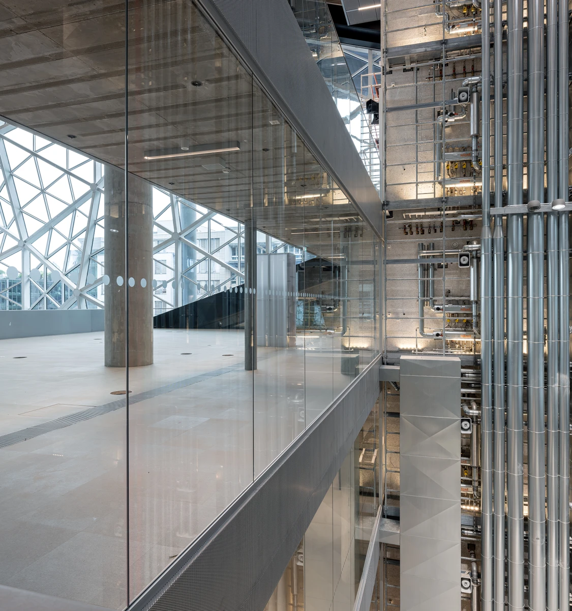 Großes, modernes Atrium mit Glasfassade und einer komplexen, sichtbaren Stahl- und Technikinstallation.