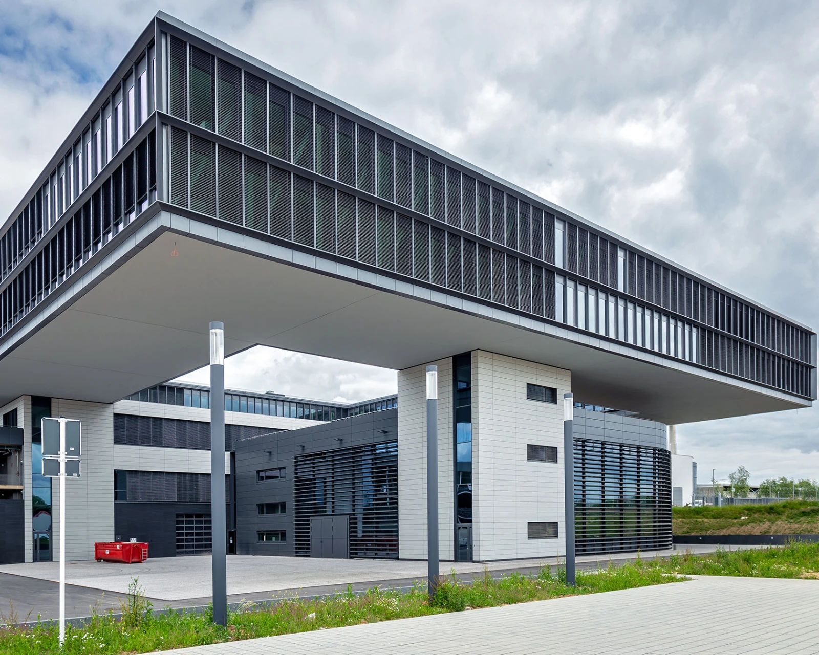 Modernes Gewerbegebäude mit langem, horizontalen Anbau. Die Fassade besteht aus Glas und dunklen Rahmen; der Bau steht vor einem bewölkten Himmel.