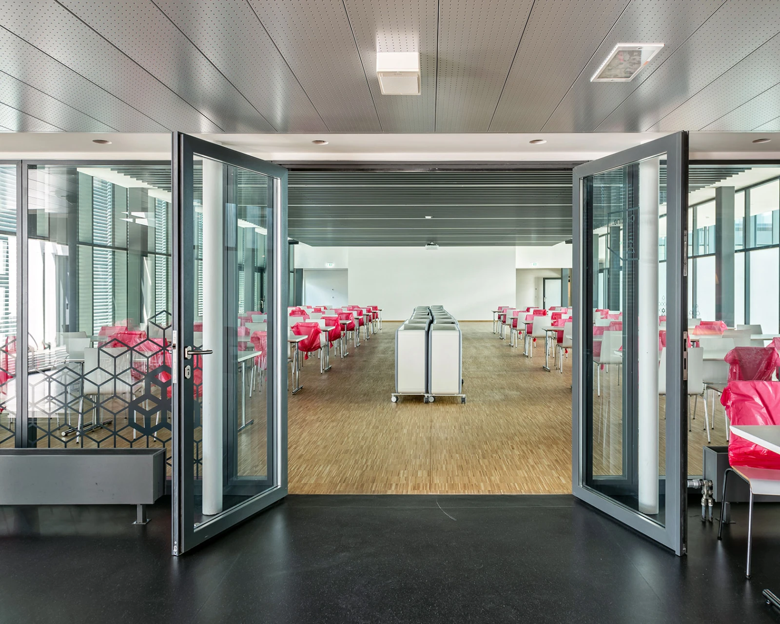 Durchgehende Glasfront führt in einen großen Saal mit zahlreichen Tischen und zentralen Service-Einheiten für Veranstaltungen.