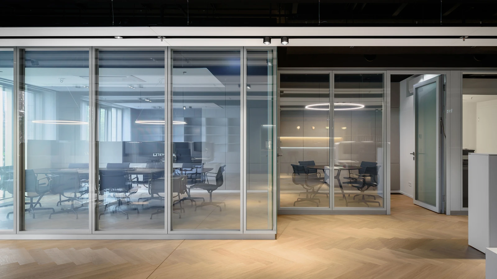 Modernes Bürodesign mit durchgehenden, transparenten Glaswänden, die mehrere, funktional getrennte Arbeitsbereiche umschließen.