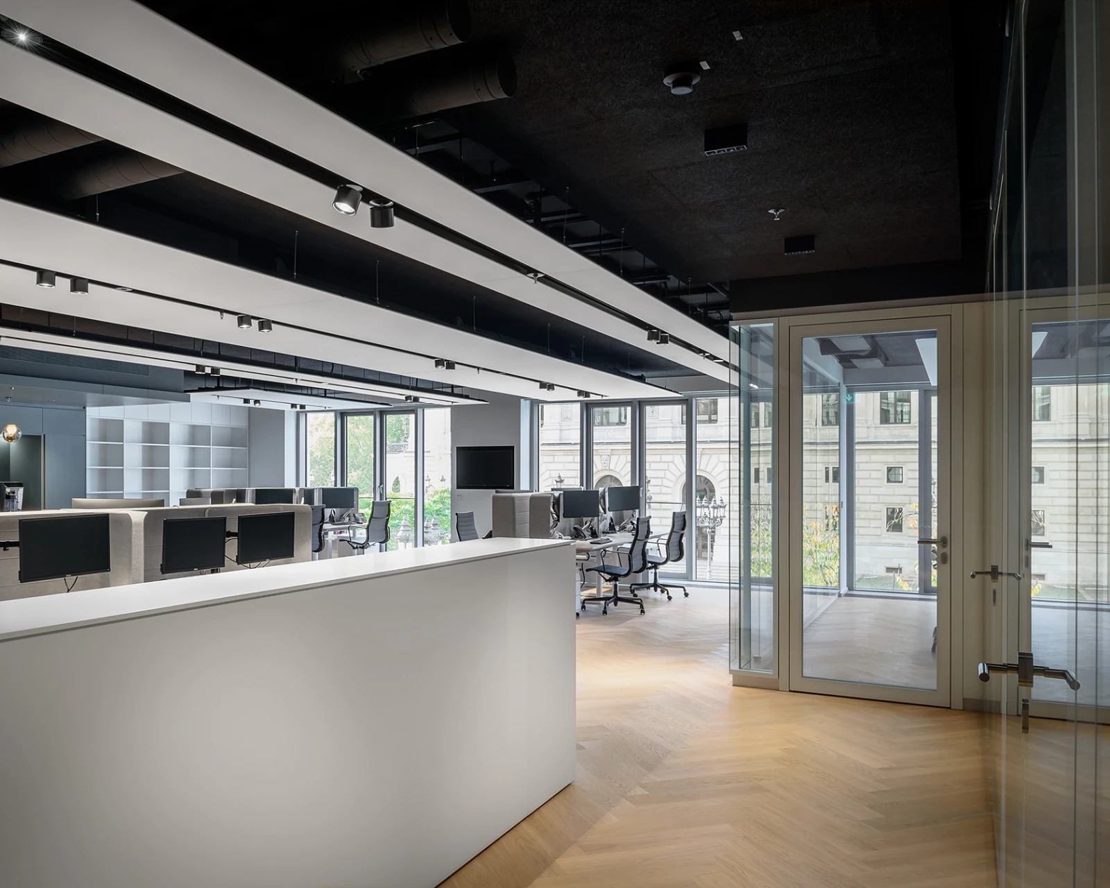 Moderner, offener Arbeitsbereich mit weißem Tresen und Schreibtischen. Große Glasfronten lassen Licht und städtischen Ausblick in den Raum.