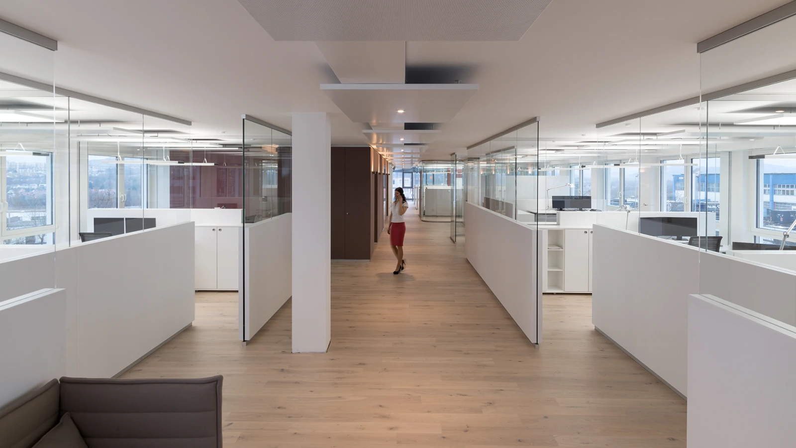 Modernes Bürointerieur mit geschlossenen Glasakustikwänden. Der helle Flur mit Holzboden wird von weißen, modernen Trennwänden eingerahmt.