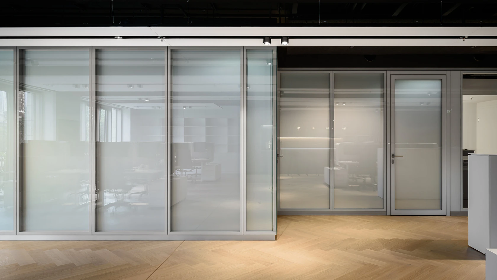Moderne, geteilte und durchscheinende Glastrennwände in einem Bürointerieur. Die Trennwände wirken strukturiert und schaffen visuelle Abgrenzung.