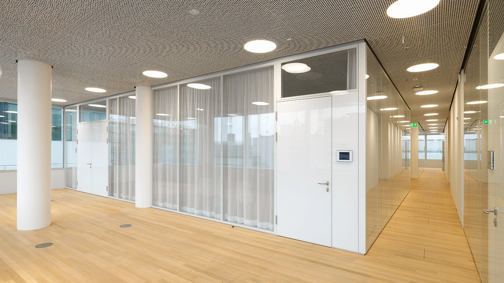 Heller, moderner Büroflur mit holzfarbigem Boden und weißem, teiltransparentem Trennwandsystem. Der Flur wird von kreisrunden Leuchten beleuchtet.