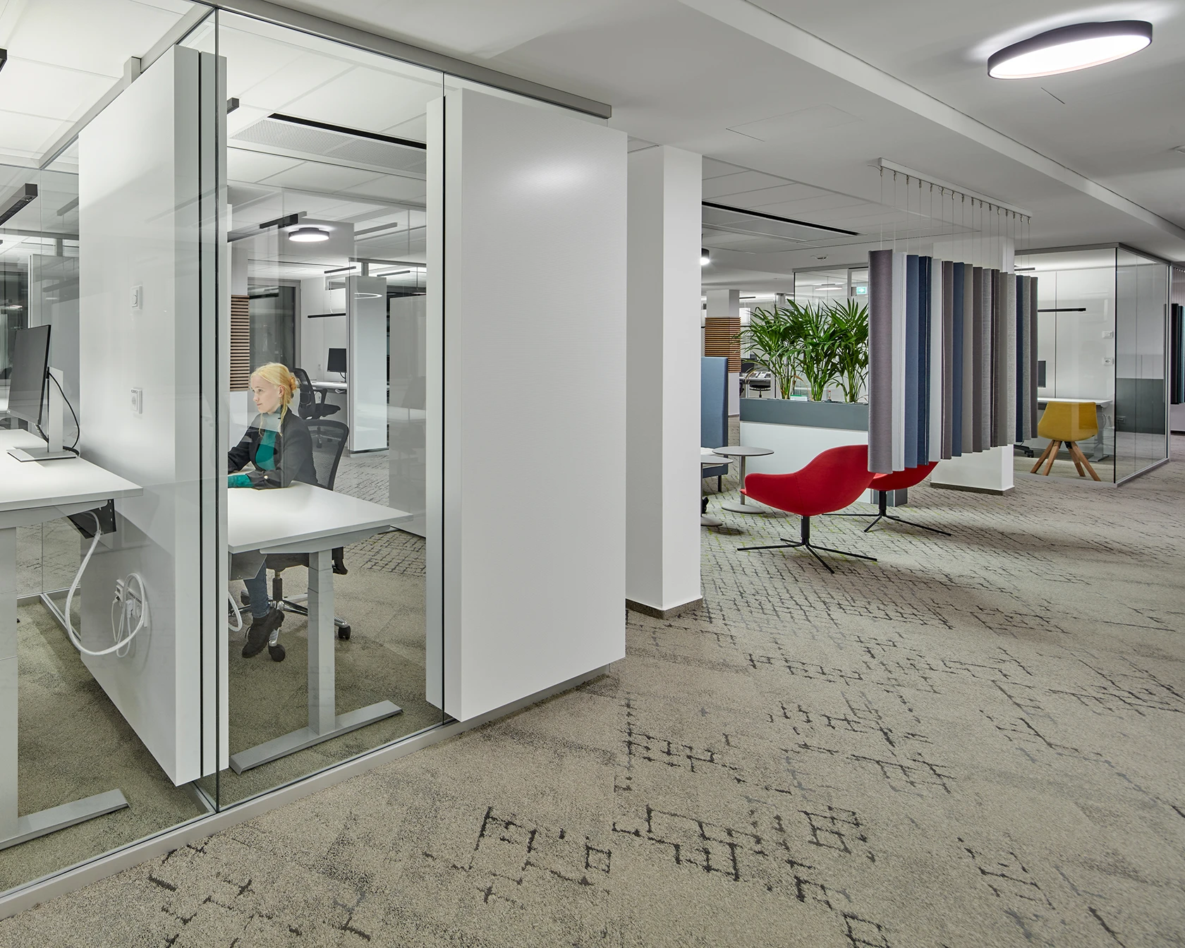 Modernes, offenes Bürointerieur mit vielen Glaswänden, hellen Arbeitsplätzen und Mitarbeitern.