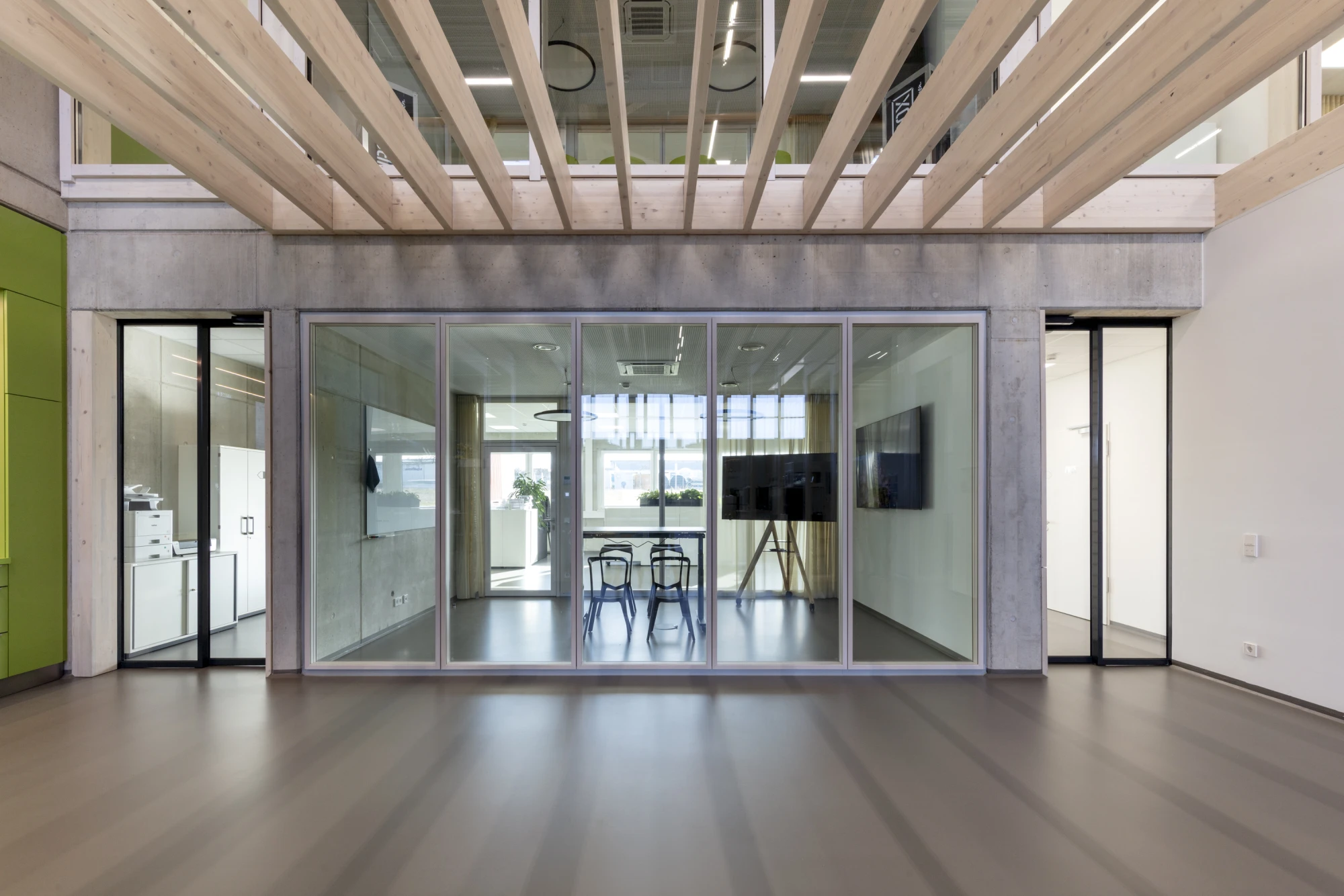 Modernes Bürodesign: Hölzerne Deckenkonstruktion, Betonelemente und eine große Glasfront trennen den Arbeits- und Gemeinschaftsbereich.