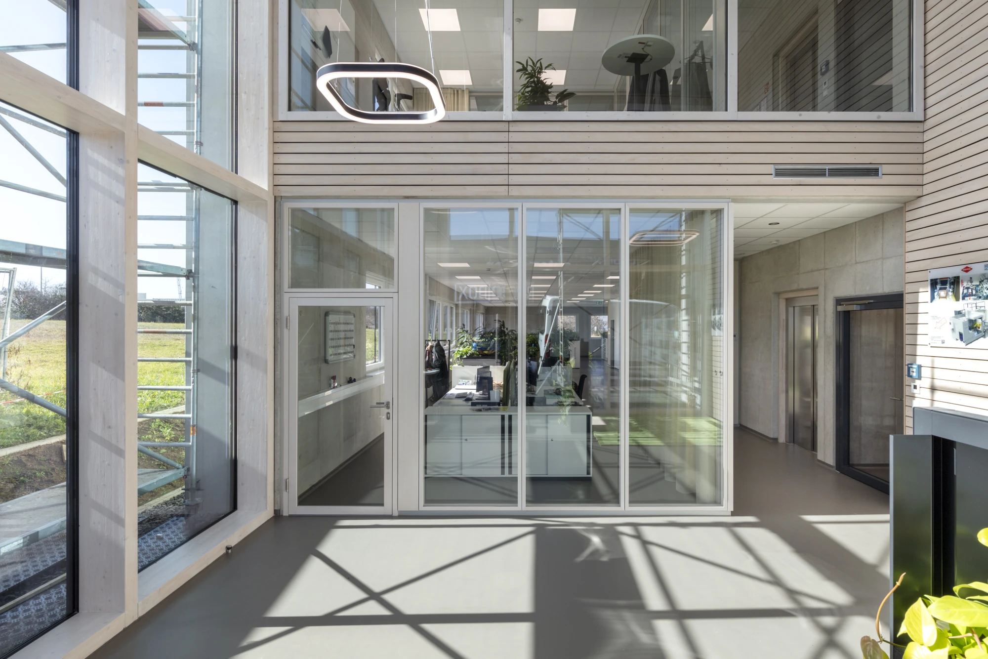 Heller, moderner Büroeingang mit weitläufiger Glasfassade. Die transparenten Türen führen in den Empfangsbereich mit industriellem Design.