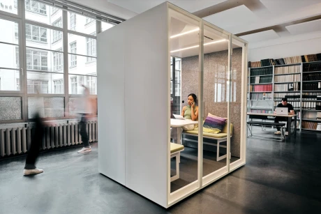 Moderne, weiße Kabine als Arbeitsbereich in einem großen, hellen Büro. Zwei Personen arbeiten konzentriert an Laptops.