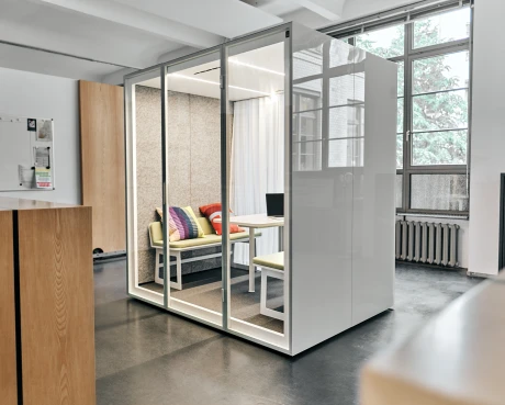 Glasfront-Teambox in modernem Büro mit Sofa, Tisch und großen Fenstern.
