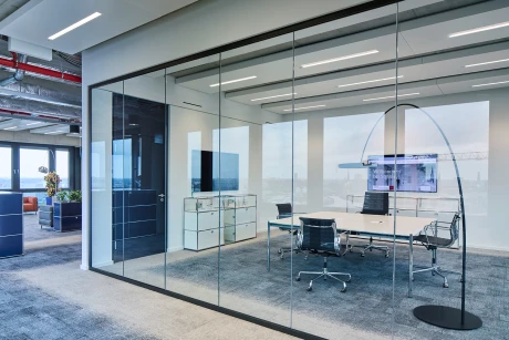 Modernes Büro mit Glastrennwand, Konferenztisch und Blick auf die urbane Skyline.