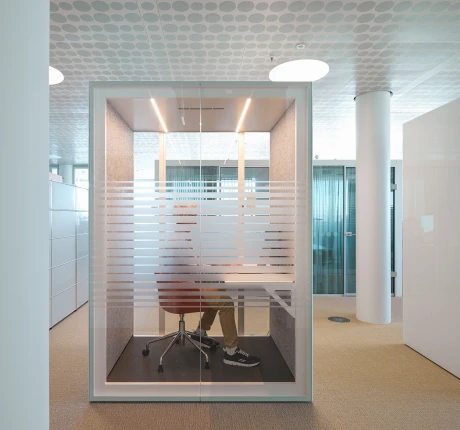 Eine Person sitzt in einem modernen, durchsichten Büro-Modul mit Schreibtisch. Das Teamarbeitskonzept im Büro.