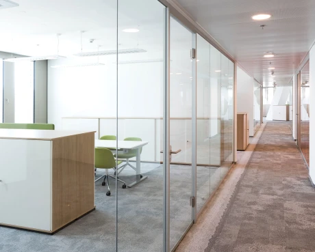 Moderne Büro-Architektur: Ein langer Flur mit transparenten Glas-Trennwänden und hellen, modular gestalteten Arbeitsbereichen.